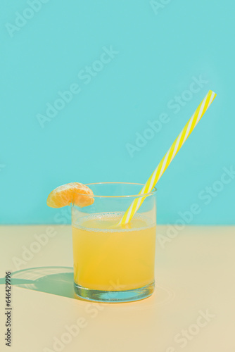 Tangerine juice in a glass with slice and straw. Turquoise and beige background. Minimalism.