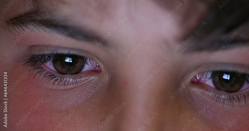 Boy macro eyes staring at screen device at night. Child browsing internet eye close-up