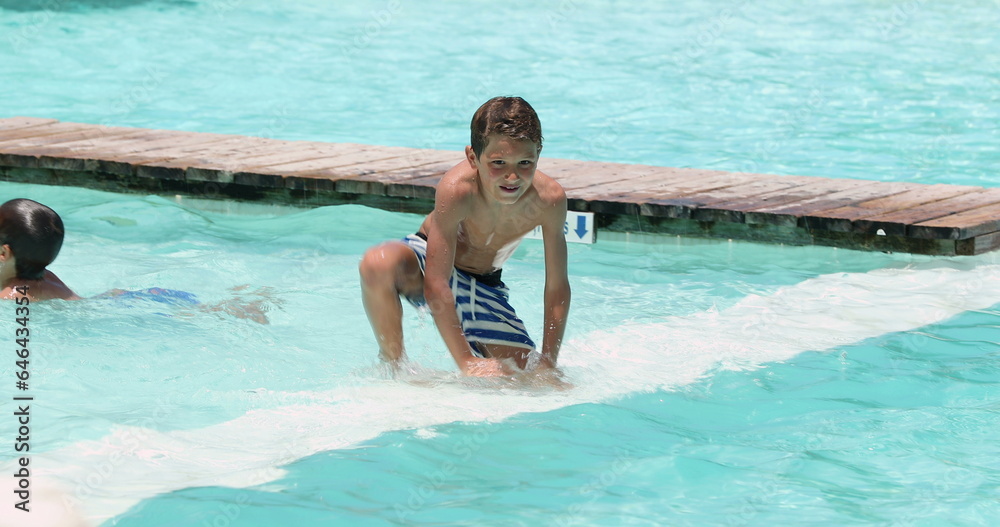 Candid family at the swimming pool enjoying summer vacations. Child jumping into pool water