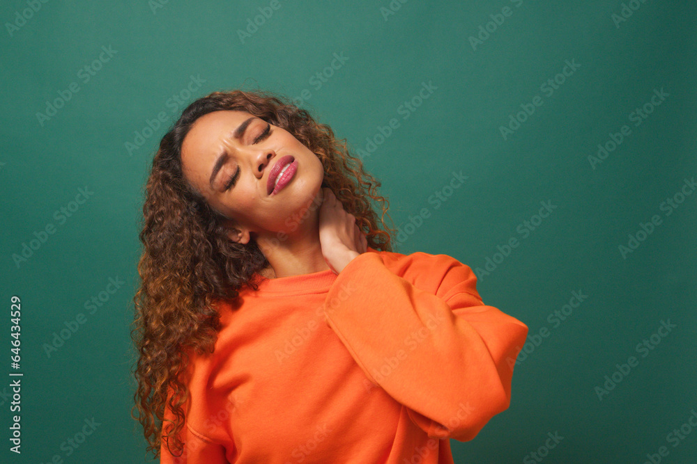 Young multi-ethnic woman rubs neck in pain, muscle ache, green studio background Young multi-ethnic woman rubs neck in pain, muscle ache, green studio background