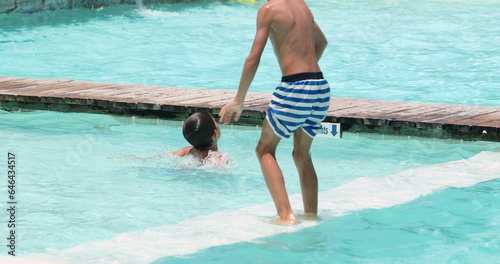 Candid family at the swimming pool enjoying summer vacations. Child jumping into pool water