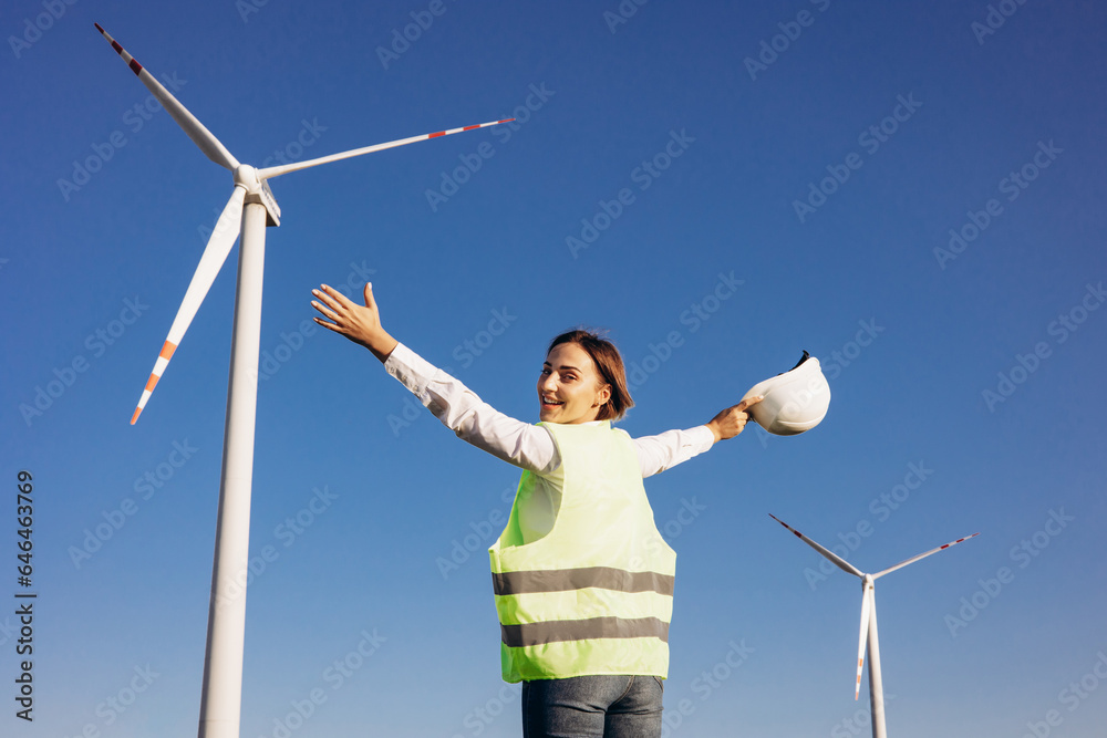 Woman engineer with helmet standing by the windmill turbines Woman engineer with helmet standing by the windmill turbines
