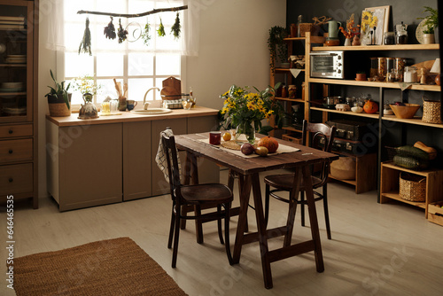 Part of spacious kitchen of large cottage or country house with wooden, chairs standing around table, shelves with vegetables and kitchenware