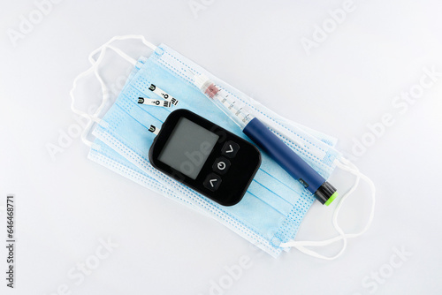 Diabetes day, electronic blood sugar test and insulin pen on fabric mask, top view
