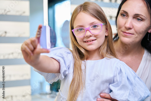Pleased child choosing lenses for her eyeglasses in optical shop