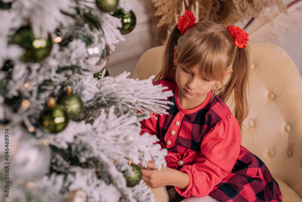 A girl in a red dress looks at the Christmas tree. Christmas holidays.