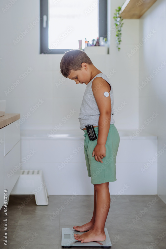A young boy with diabetes weighing himself on bathroom scale A young boy with diabetes weighing himself on bathroom scale