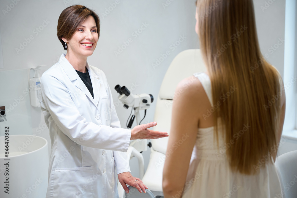 Female doctor offers patient to stay in a gynecological chair Female doctor offers patient to stay in a gynecological chair