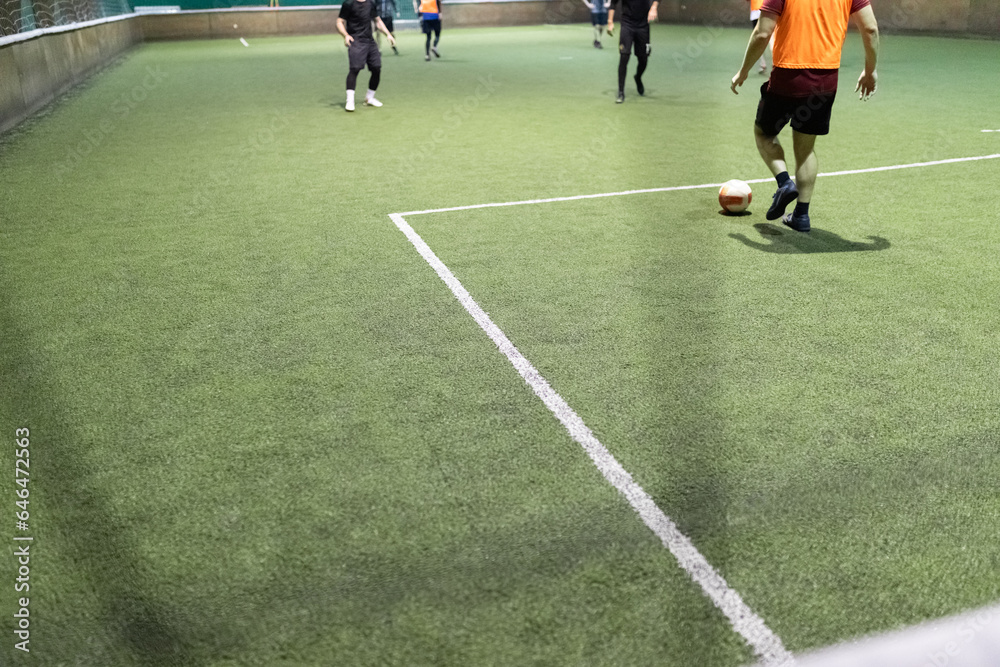 Obraz premium Futsal game with men players on artificial turf field court indoors.