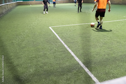 Futsal game with men players on artificial turf field court indoors.
