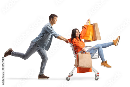 Young man pushing a female with shopping bags inside a shopping cart