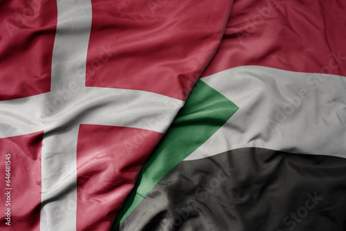 big waving national colorful flag of denmark and national flag of sudan .