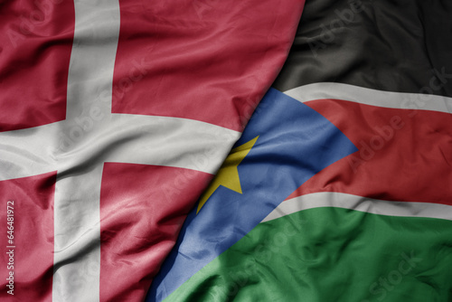 big waving national colorful flag of denmark and national flag of south sudan .