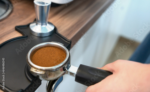 The barista's hand holds a holder with ground fresh coffee for making coffee in a coffee machine. Close-up. Selective focus.