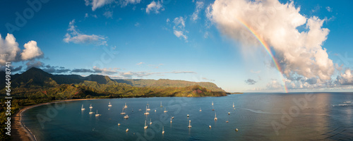 Aerial view of rainbow and sunlit clouds over the mountain peaks of Na Pali coast across Hanalei Bay on Kauai