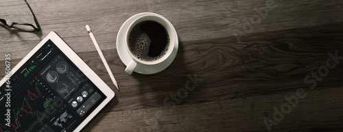 top view Cup of coffee with digital tablet computer, business finance charts and pen on wood background.
