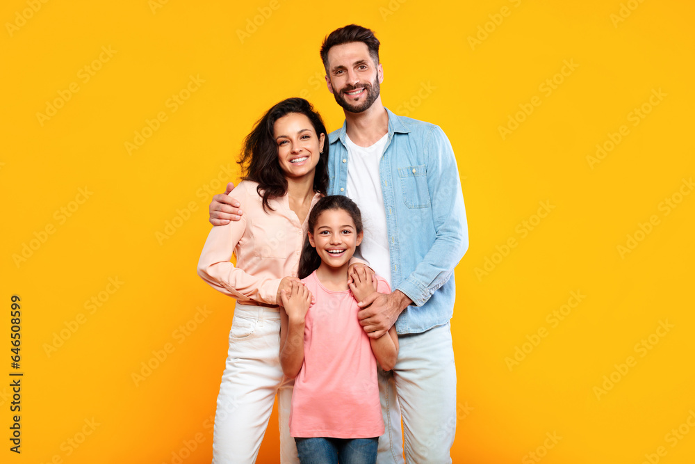 Happy european family of three hugging and smiling to camera, posing together over yellow studio background Happy european family of three hugging and smiling to camera, posing together over yellow studio background