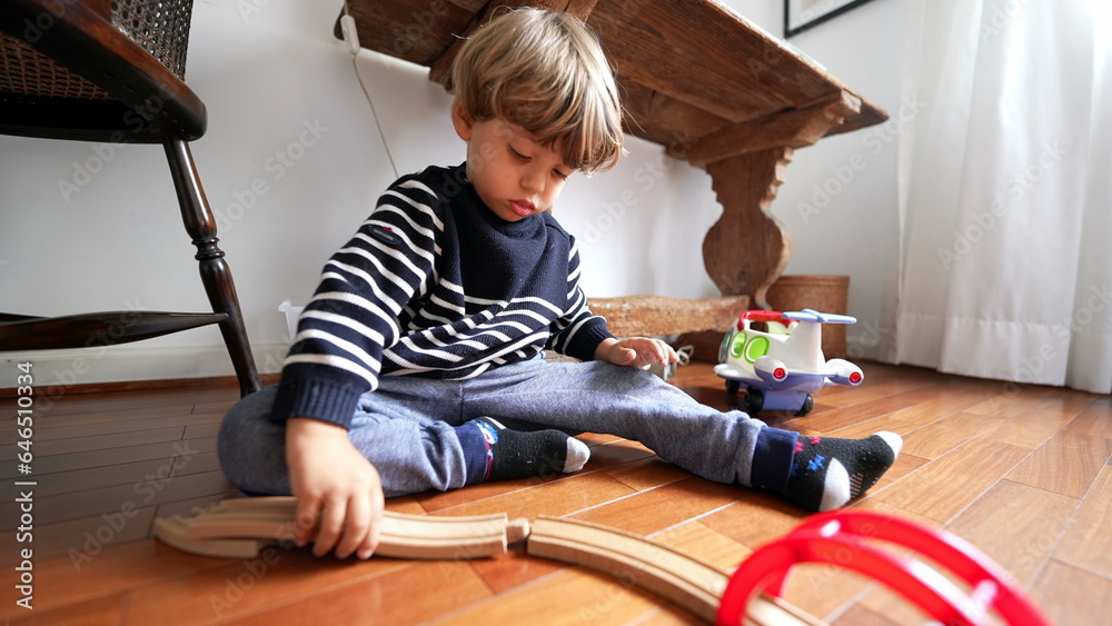 Child plays with retro toys on hardwood floor. One small boy playing indoors with train wooden tracks by himself Child plays with retro toys on hardwood floor. One small boy playing indoors with train wooden tracks by himself