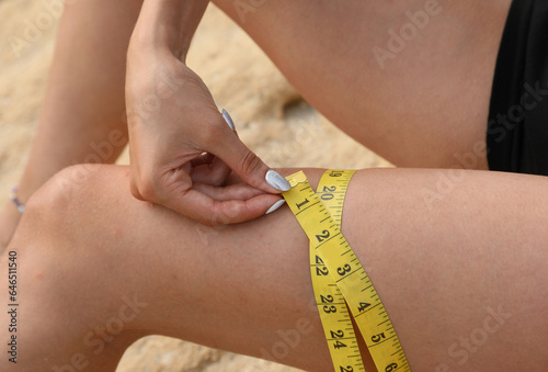 thigh of young woman measured with yellow tape measure and numbers in INCHES
