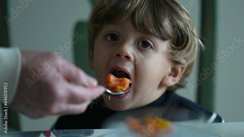 Hand feeding food to small boy  close-up face of a caucasian male child eating fruit