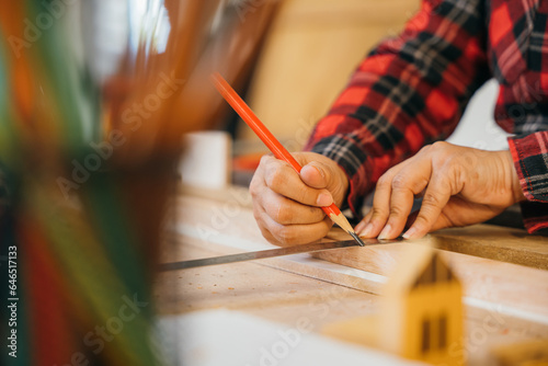 Closeup hand senior woman carpenter taking measurement of wooden plank and make in carpentry workshop, female holding ruler and use pencil drawing sign on wood at woodshop, National Carpenters Day