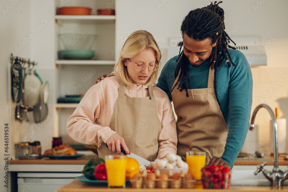 A happy interracial affectionate couple is cooking together at home.