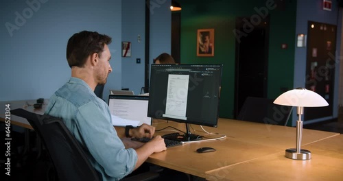 A man working in a modern office space, in front of a large monitor, using a mouse on the desk