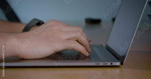 Close-up of a man's hands typing on a laptop keyboard against a blue wall