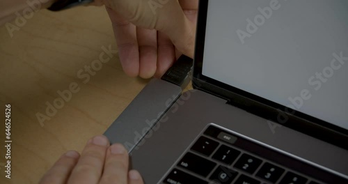 A close-up of a hand connecting an HDMI cable through a hub to a laptop