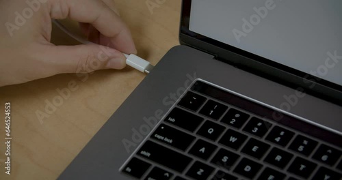 A close-up of a hand connecting a Type-C charger to a laptop