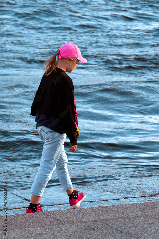 A teenage girl 12-14 years old walks along the stone embankment of the ...