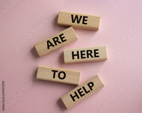 We are here to help symbol. Concept words we are here to help on wooden blocks. Beautiful pink background. Business and we are here to help concept. Copy space.