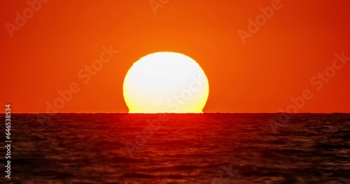 Sunset video for background. Bright orange sunset over water, huge disk of sun goes beyond horizon, as if plunging into water. Nature weather orange sky. Grey clouds. Cinematic video with no people