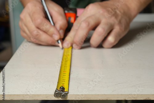 A worker makes markings using a measuring tape and a pencil.