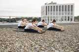 Yoga lovers folding forward on yoga mats in open air on roof