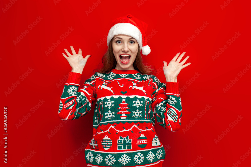 young cute girl in christmas sweater and santa hat rejoices and shouts on red background young cute girl in christmas sweater and santa hat rejoices and shouts on red background