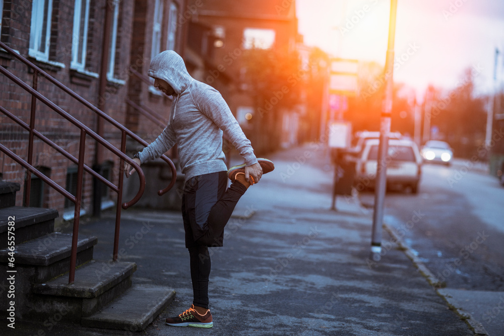 Young man warming up and stretching before jogging during winter in the city