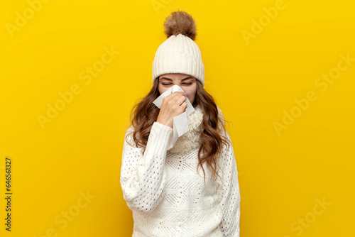 sick girl in warm soft winter clothes with runny nose in napkin on yellow isolated background, cold woman photo