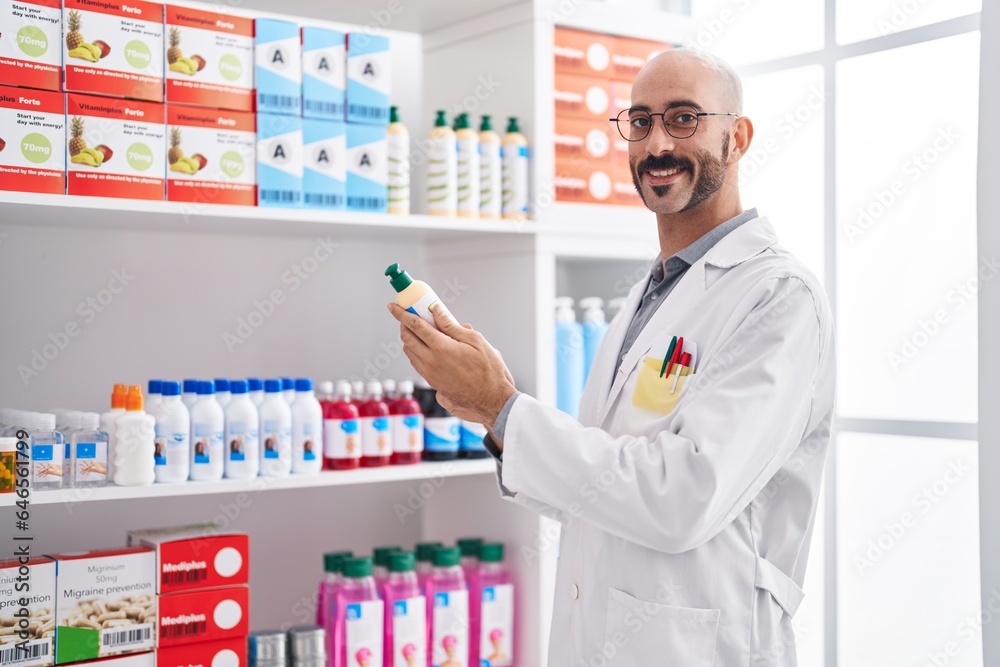 Young hispanic man pharmacist smiling confident holding bottle at pharmacy