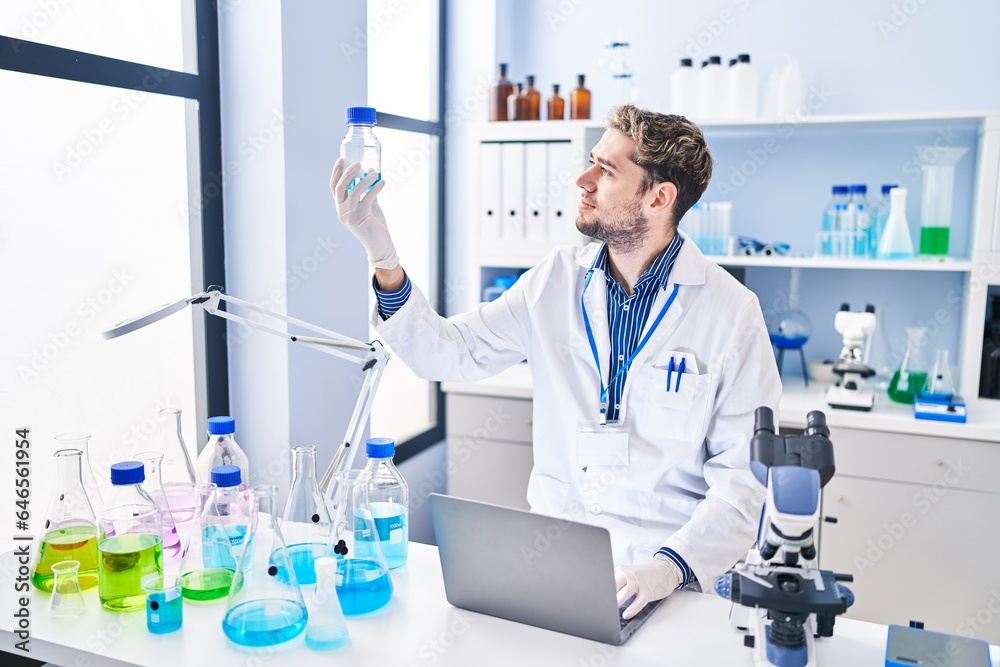Young man scientist using laptop holding bottle at laboratory Young man scientist using laptop holding bottle at laboratory
