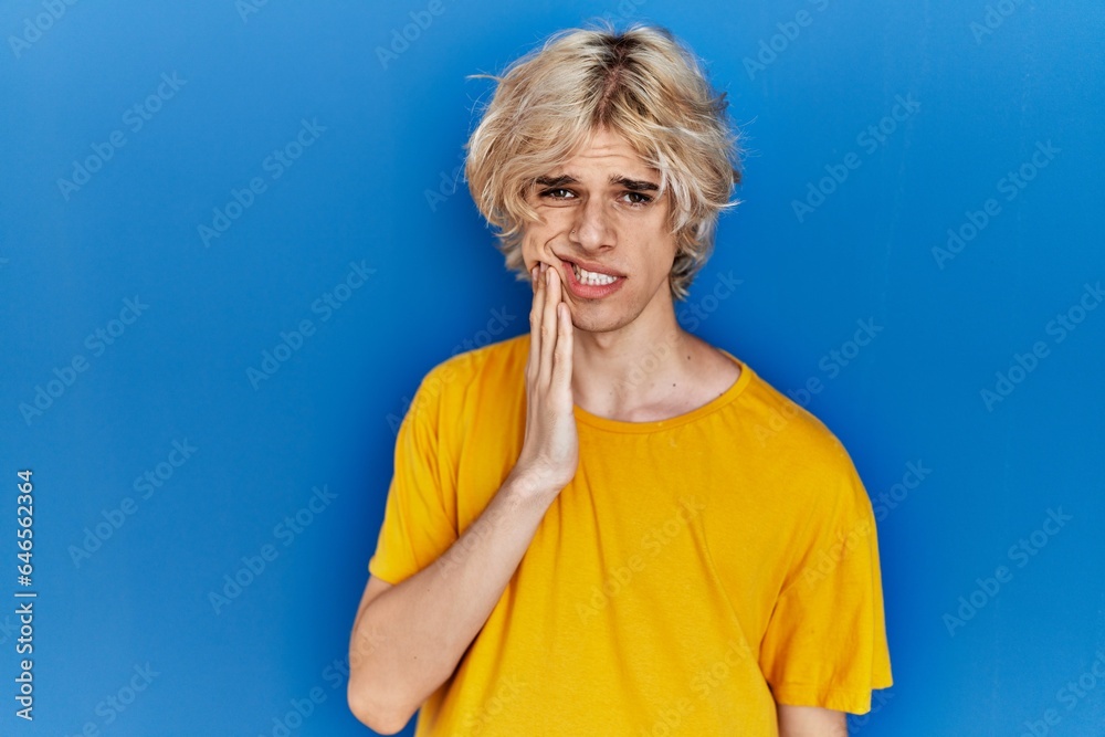 Young modern man standing over blue background touching mouth with hand with painful expression because of toothache or dental illness on teeth. dentist Young modern man standing over blue background touching mouth with hand with painful expression because of toothache or dental illness on teeth. dentist