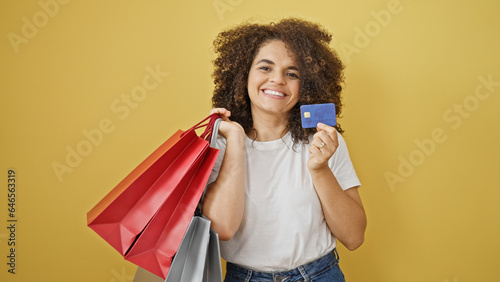 Young beautiful hispanic woman holding shopping bags and credit card smiling over isolated yellow background