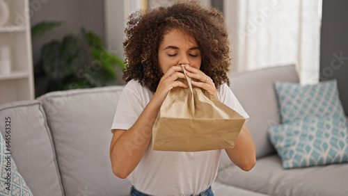 Young beautiful hispanic woman blowing air on paper bag suffering panic attack at home