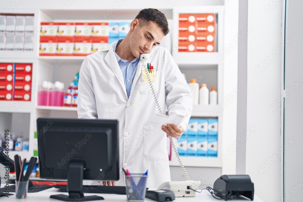Young hispanic man pharmacist talking on telephone reading prescription at pharmacy Young hispanic man pharmacist talking on telephone reading prescription at pharmacy