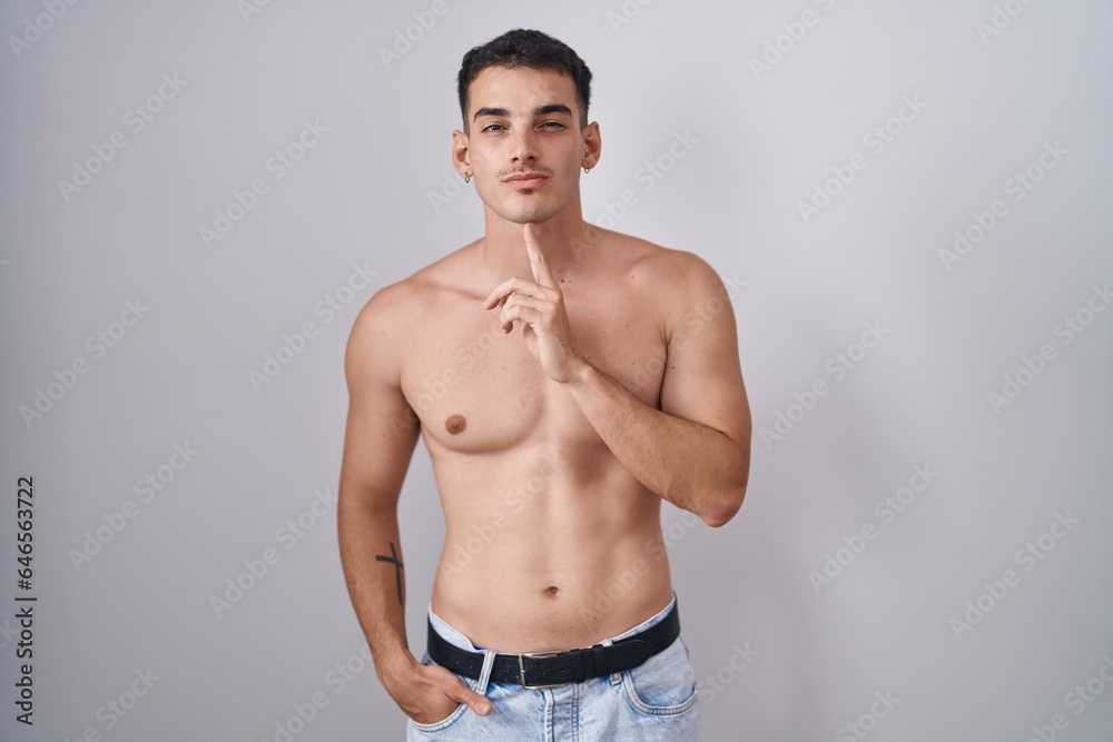 Handsome hispanic man standing shirtless thinking concentrated about doubt with finger on chin and looking up wondering