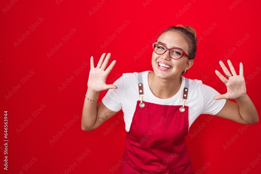 Young hispanic woman wearing waitress apron over red background showing and pointing up with fingers number ten while smiling confident and happy. Young hispanic woman wearing waitress apron over red background showing and pointing up with fingers number ten while smiling confident and happy.