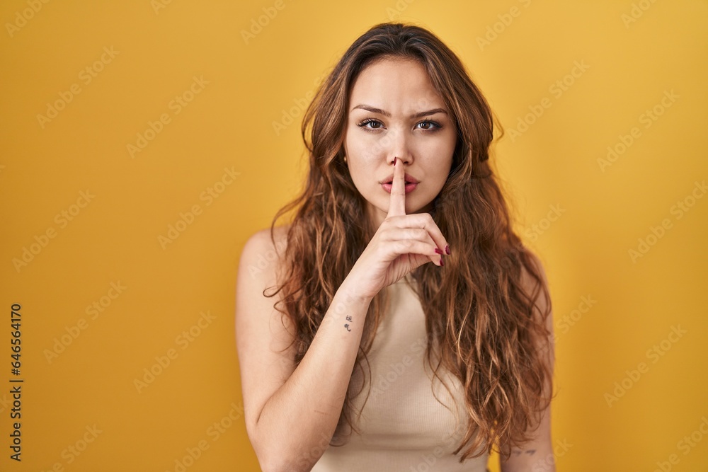 Young hispanic woman standing over yellow background asking to be quiet with finger on lips. silence and secret concept. Young hispanic woman standing over yellow background asking to be quiet with finger on lips. silence and secret concept.