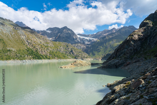 Alpe Gera lake and Fellaria Glacier with waterfall in the background, blue sky with clouds, soft warm light. mountains landscape