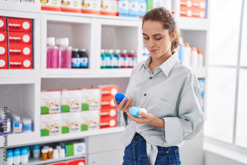 Young woman customer holding deodorant bottles at pharmacy