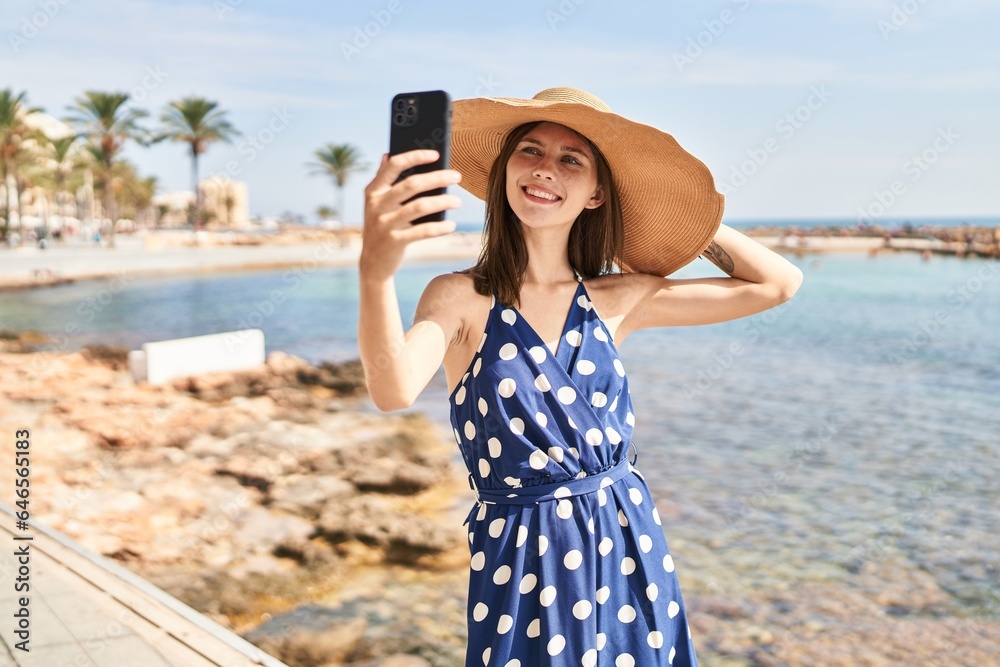 Young blonde woman tourist wearing summer hat make selfie by smartphone at beach